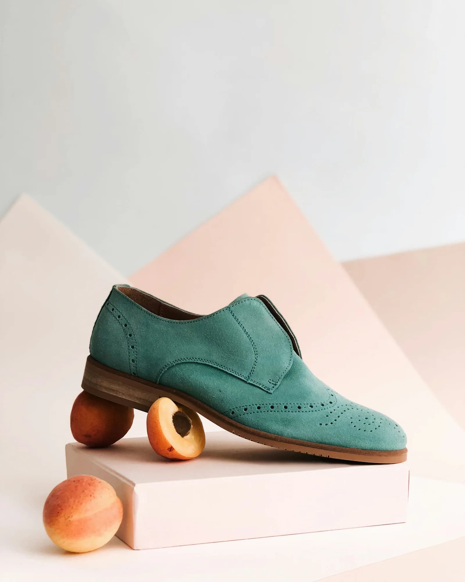 Teal suede loafer displayed on a pink geometric background