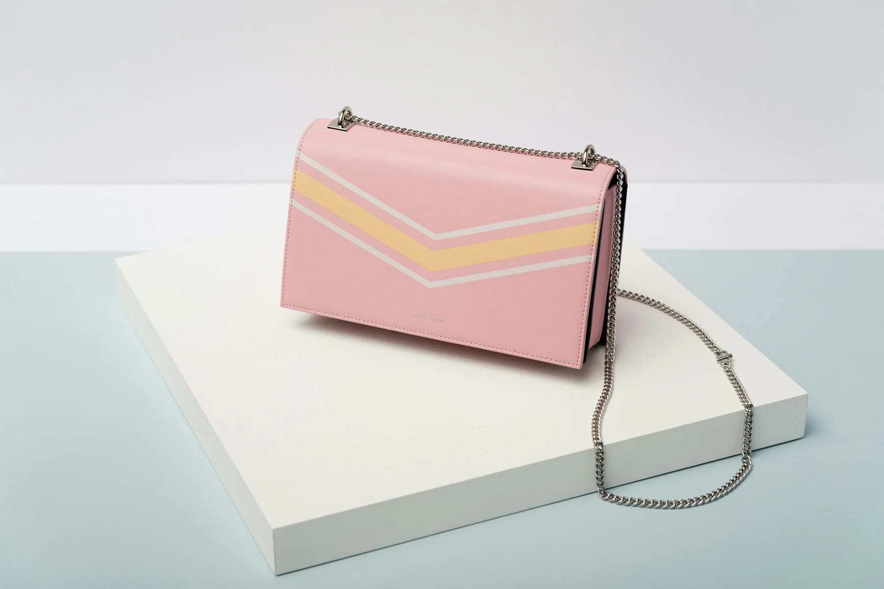 Pink crossbody bag with a chevron flap on a white box
