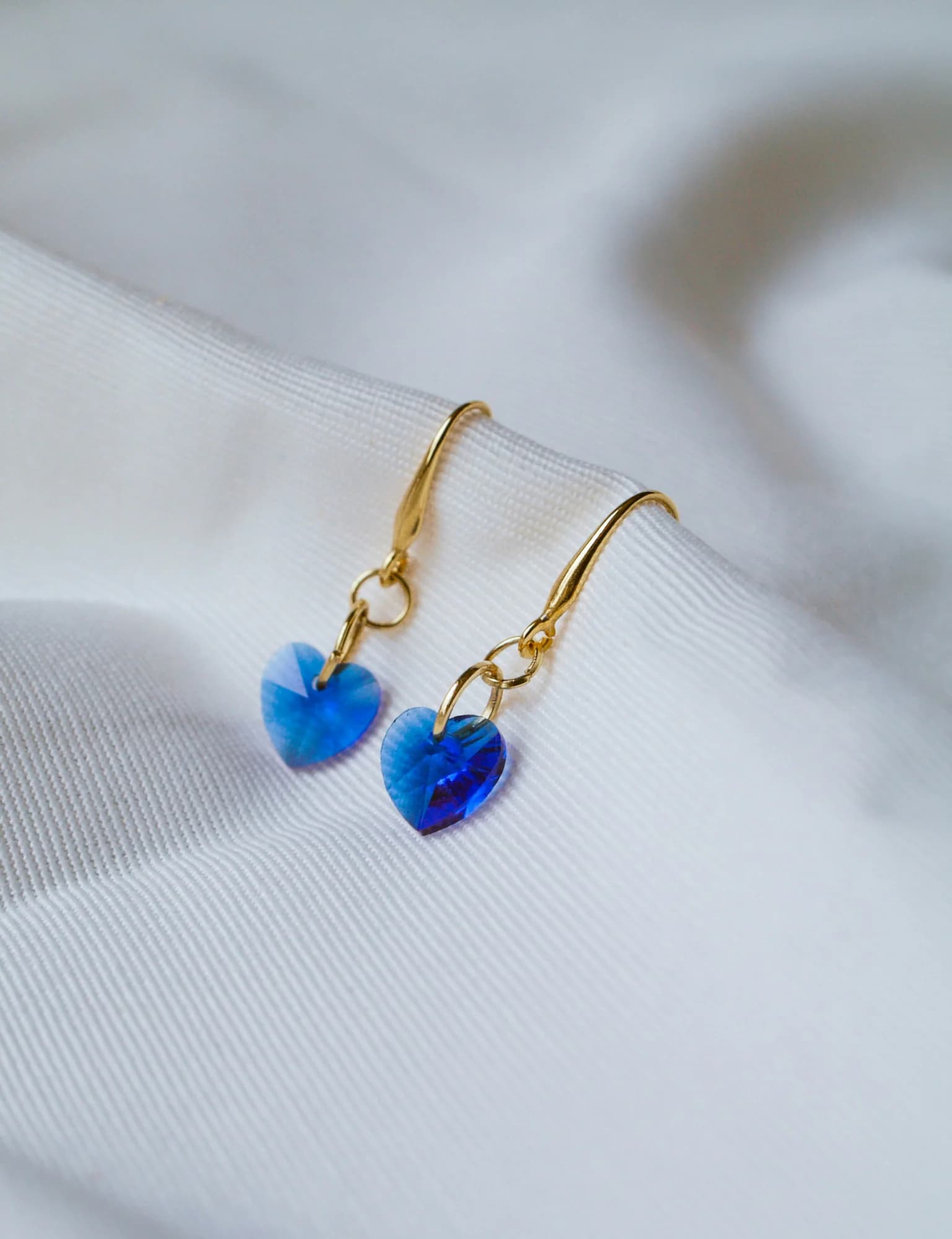 Blue crystal heart drop earrings on white fabric