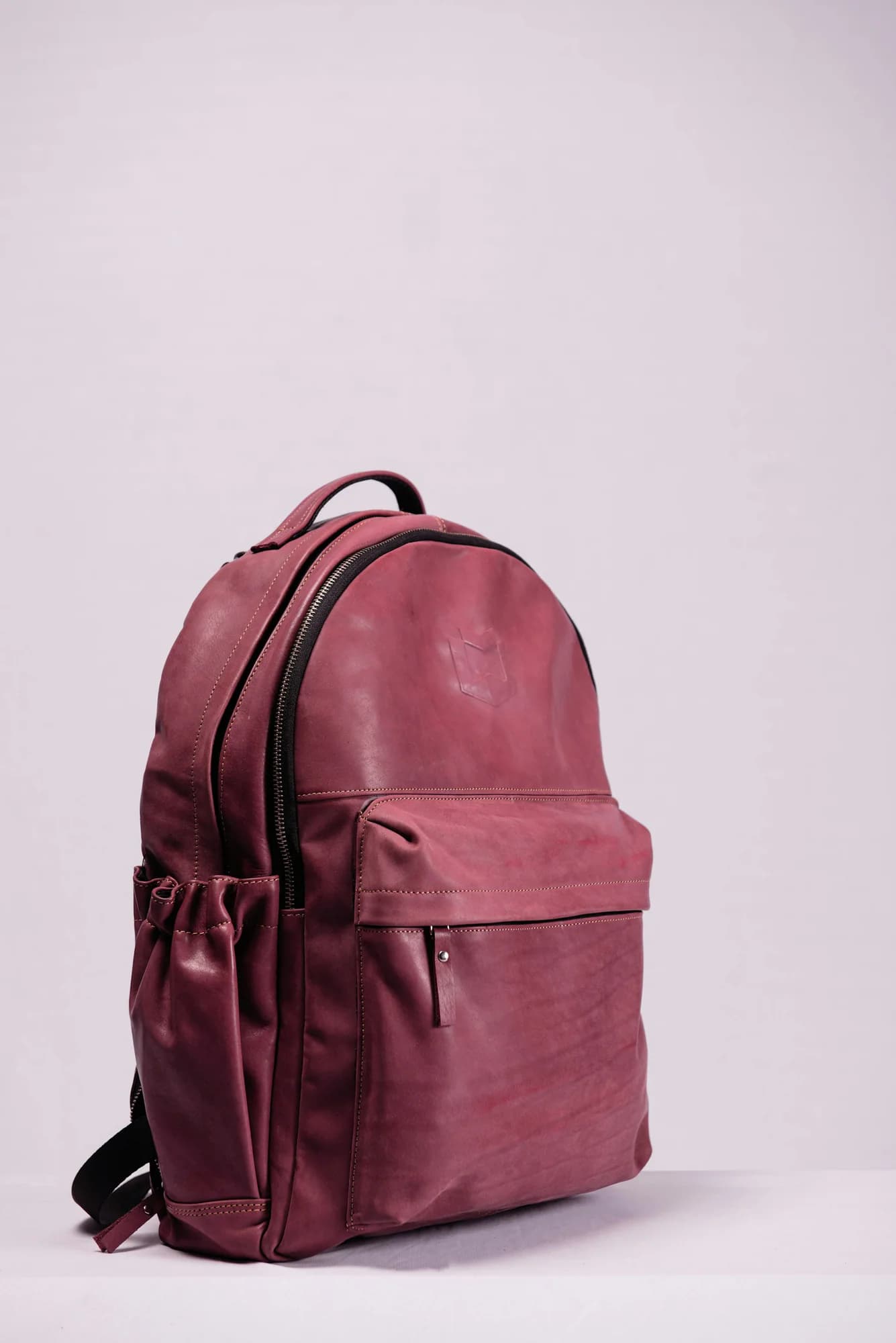 Burgundy leather backpack against a pink background