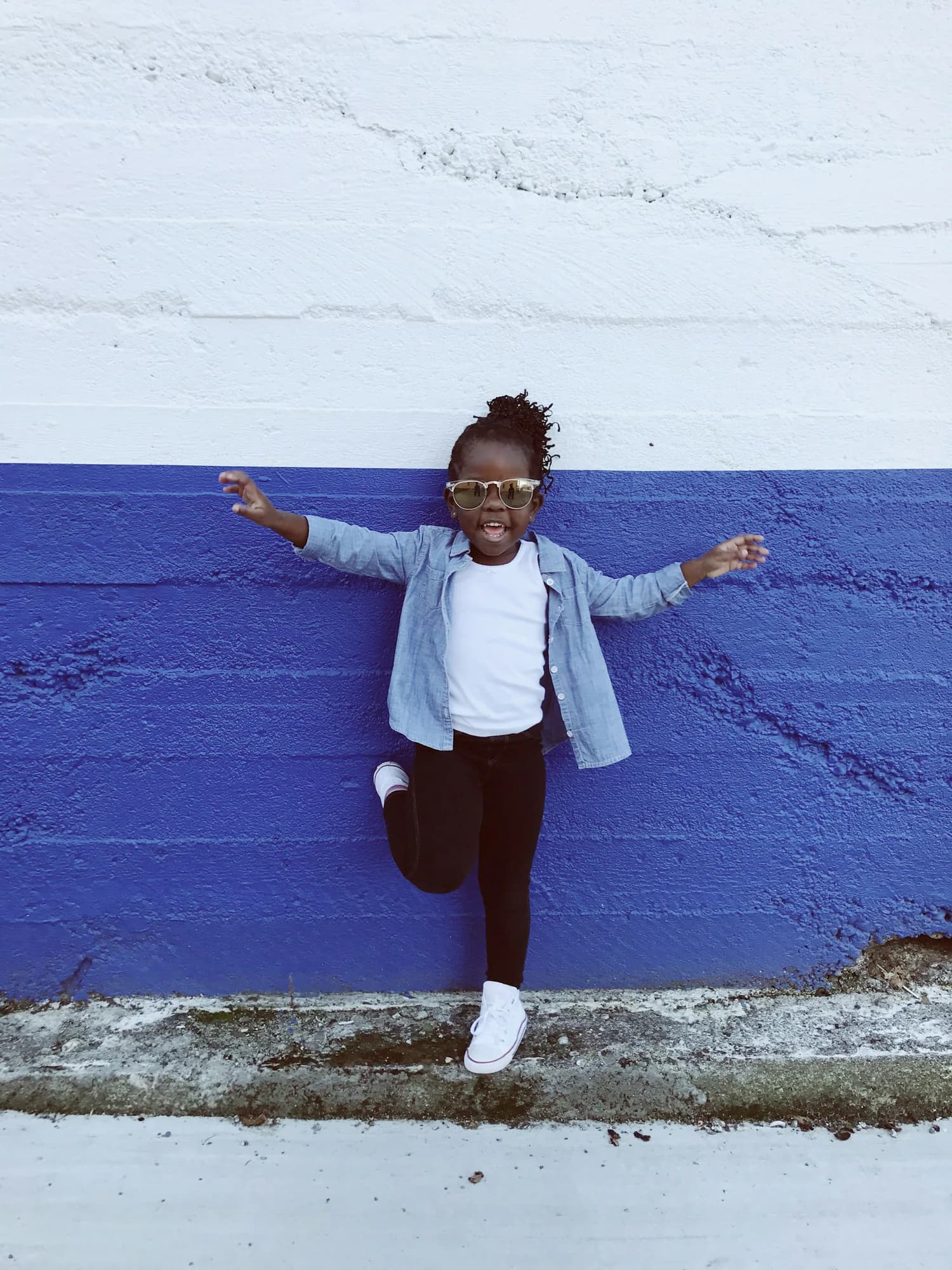 Girl in a light denim jacket jumping against a blue wall