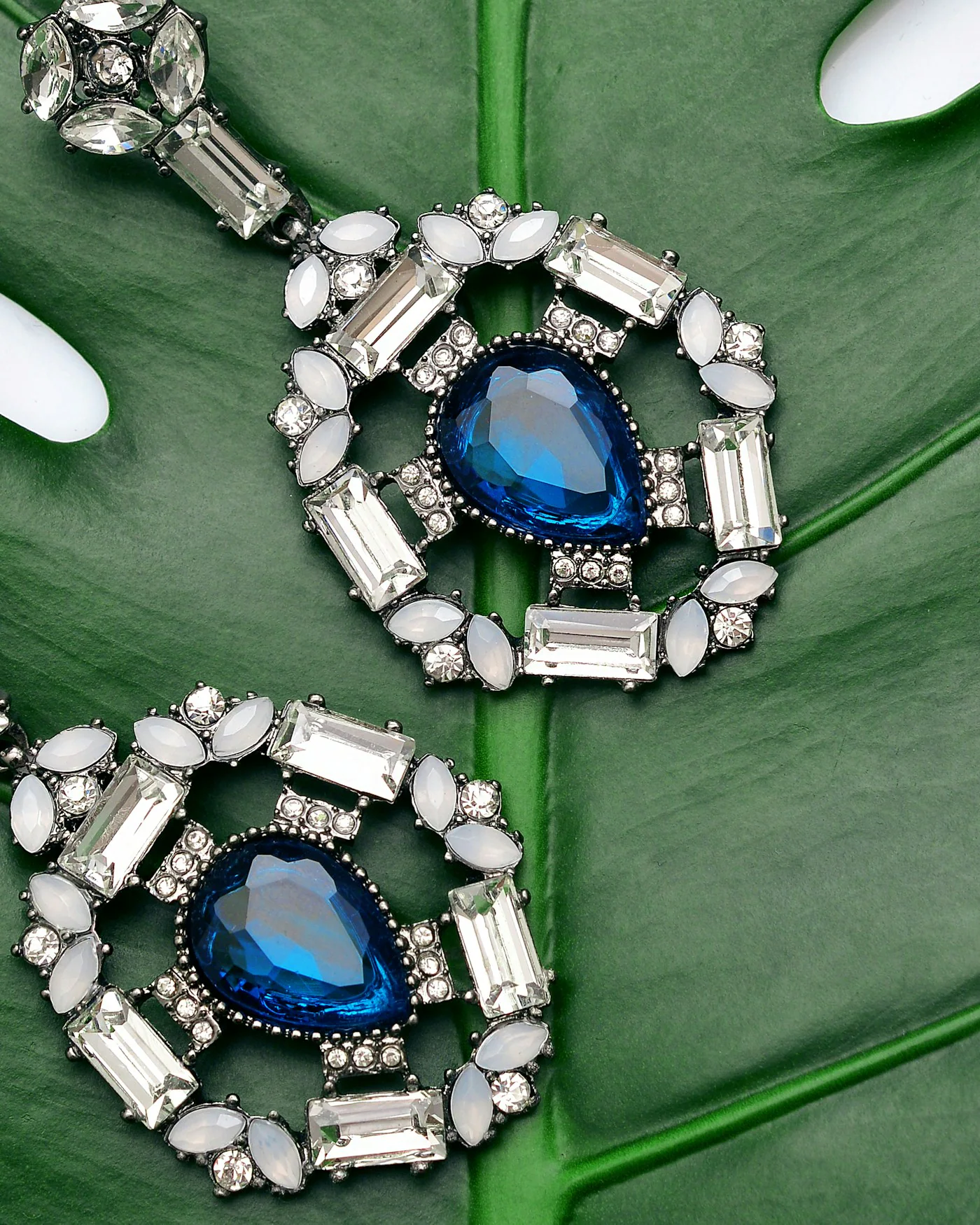 Sapphire drop earrings resting on a green leaf — detail