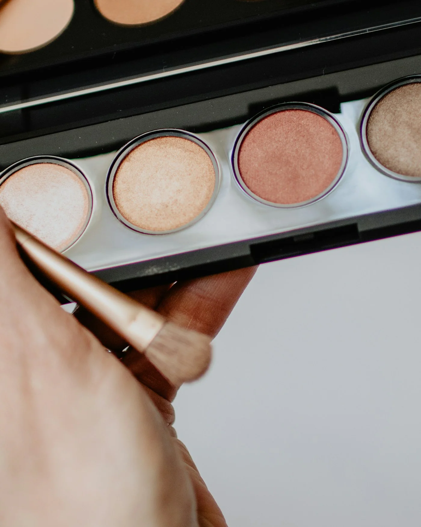 Hand holding a neutral eyeshadow palette with a brush — detail
