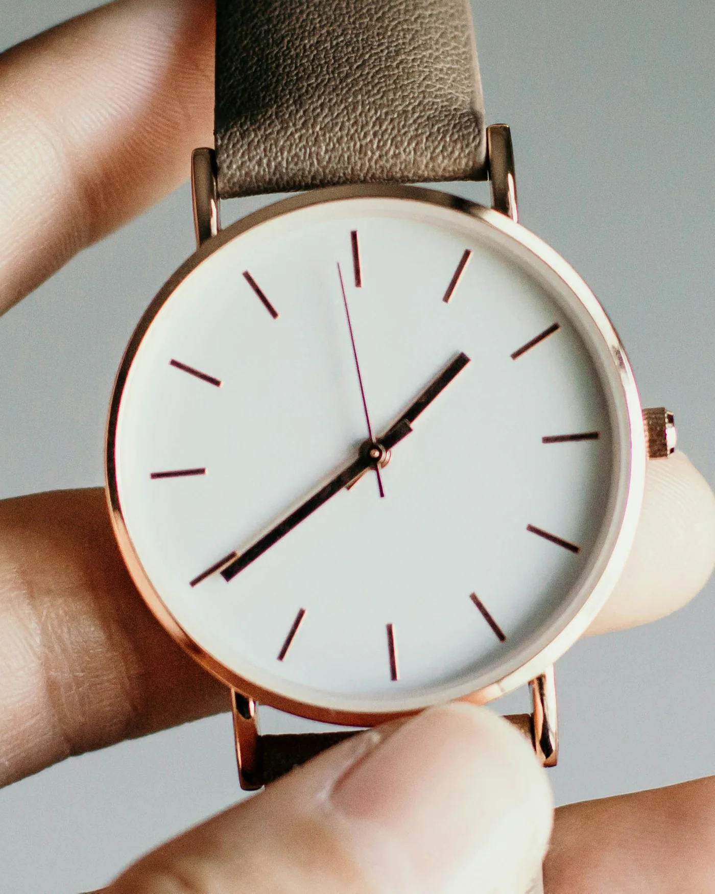 Hand holding a minimalist watch with a white dial and tan strap — detail