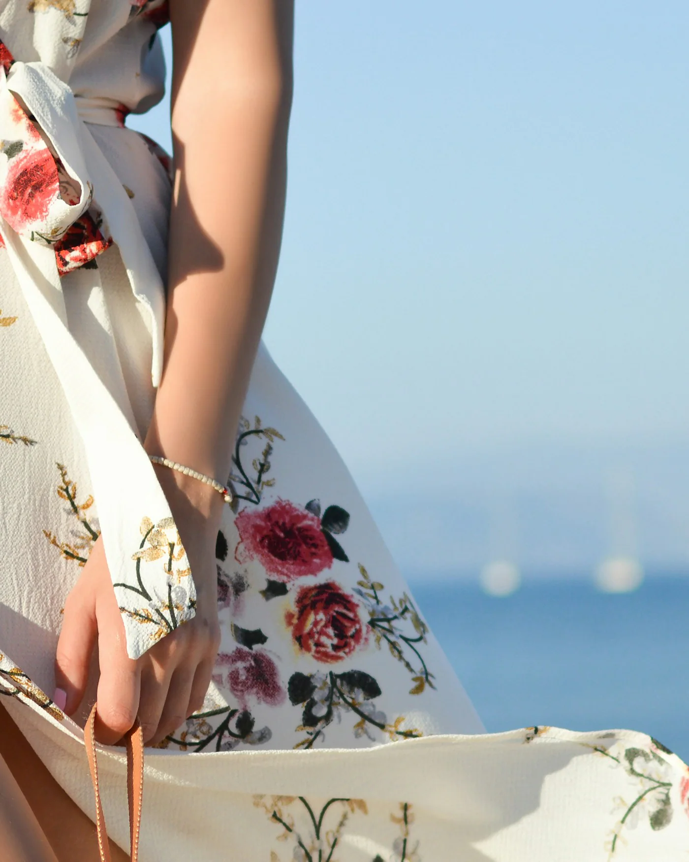 Woman wearing a white floral wrap dress by the sea — detail