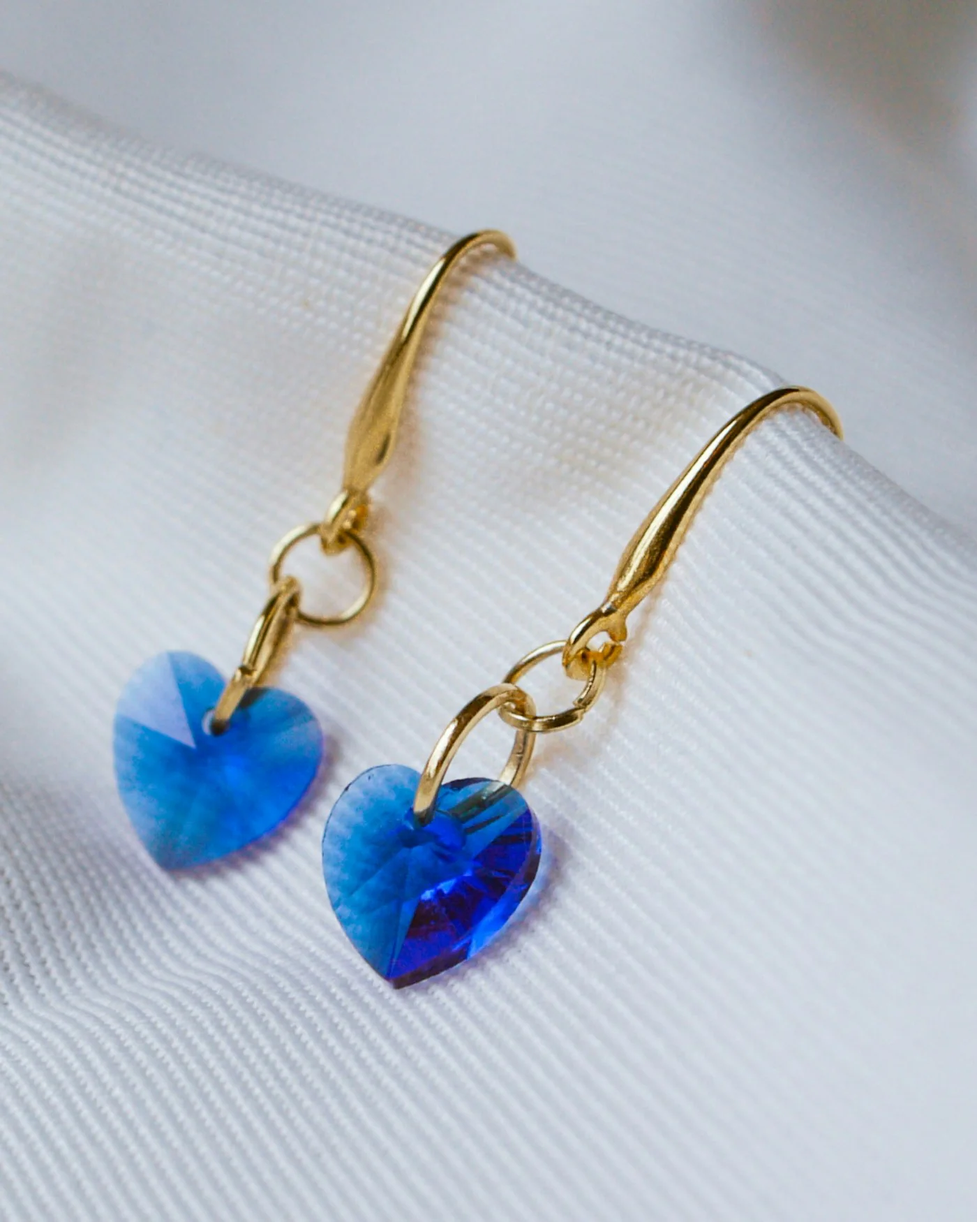 Blue crystal heart drop earrings on white fabric — detail