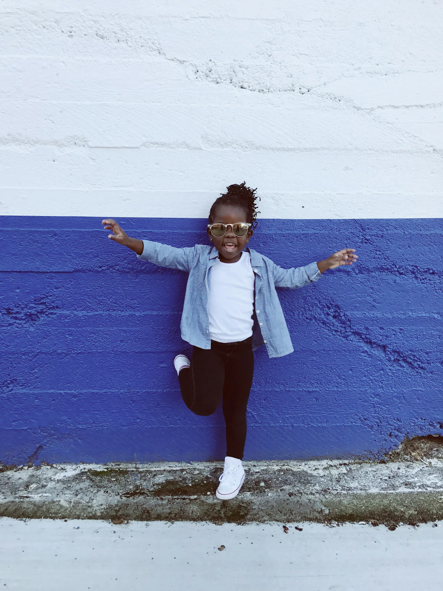 Girl in a light denim jacket jumping against a blue wall