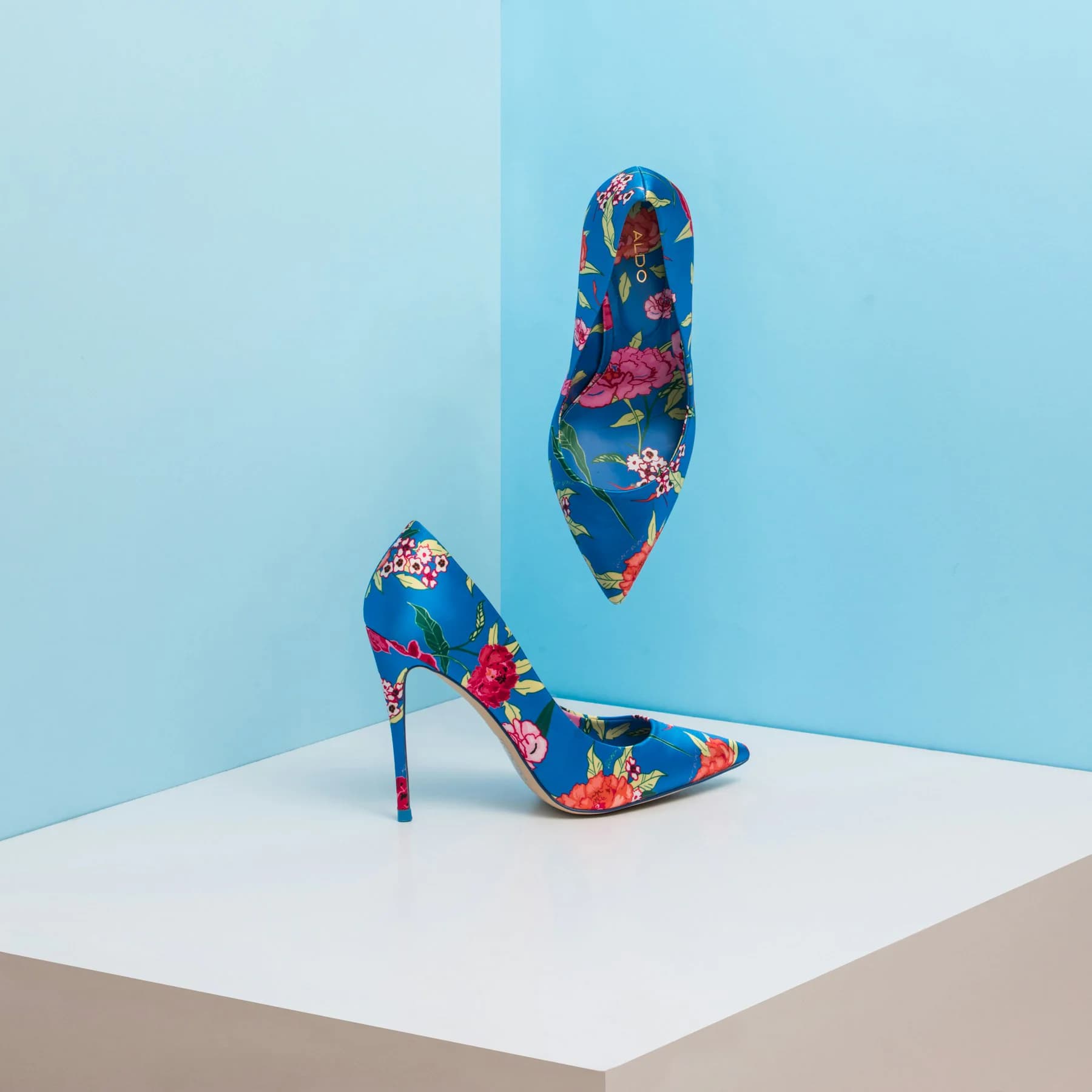 Pair of floral print stiletto heels against a blue background