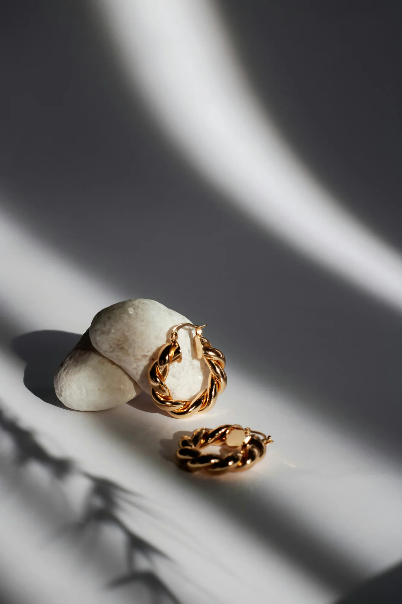 Sculpted gold hoop earrings on a white shell